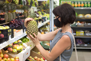 Woman buyer in a protective medical mask chooses a pineapple store.