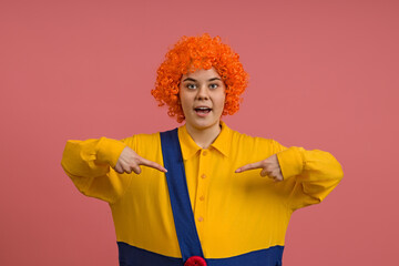 a cheerful clown in a wig and a yellow-blue suit joyfully points to himself, a colored background