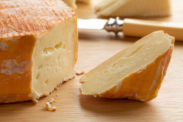 Piece of French Le Chandor cheese with an orange crust close up on a cutting board 