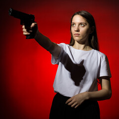 young woman with long hair in a white t-shirt takes aim with a gun on a red background