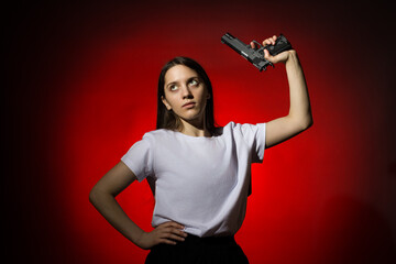 young woman with long hair in a white t-shirt with a gun on a red background
