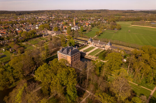 Picturesque moated castle Amerongen seen from above surrounded by gardens and park with the village town and countryside meadows in the background. Aerial Dutch nobility landscape