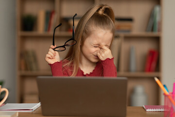 Little Girl Rubbing Eyes Holding Glasses Using Laptop At Home