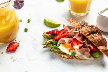 Delicious fresh breakfast served grilled bun with spinach and cheese, asparagus, jamon, ham, prosciutto and fried egg. fresh juice, Balanced diet. place for text, top view