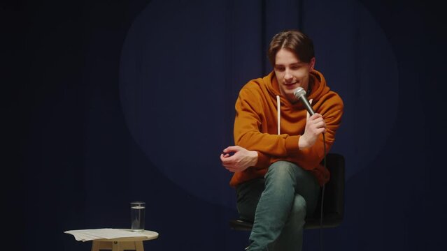 Stand-up cafe, comedy concert. Man telling jokes on stage. Male comedian speaking with audience using microphone, humorous monologue. Mentor coach training.