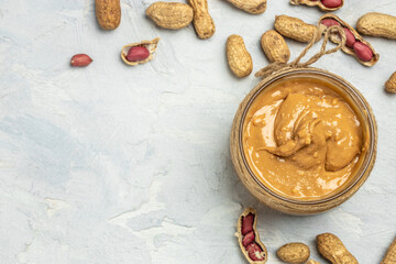 peanut paste in an open jar in spoon near creamy peanut butter peanuts scattered on a light background, place for text, top view