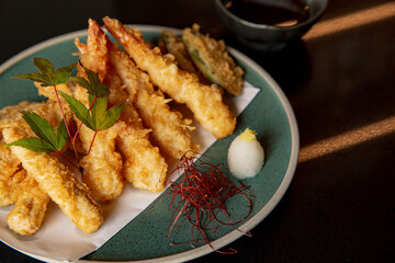Kaiseki dish, ebi fry on the fine green plate in the fine dining Japanese restaurant, dark background, side with radish and decoration.