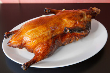 Whole roast duck Peking duck of traditional Cantonese yum-cha Asian gourmet cuisine meal food dish on the white serving plate and brown red table