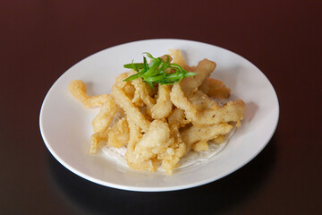 Fried salt and pepper squid of traditional Cantonese yum-cha Asian gourmet cuisine meal food dish on the white serving plate and brown red table