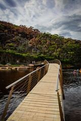 Tidal River wooden bridge at Wilson Promontory with autumn maple tree and cloudy sky view, people...