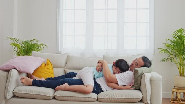 Father and son hugging on the sofa in a happy Asian family. love and care, enjoying time together, Father's Day. Parents 44 with Children 7 years