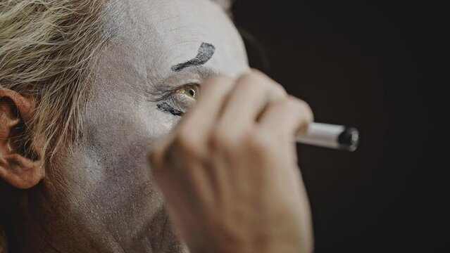 Professional mime puts on theatrical makeup with black liner