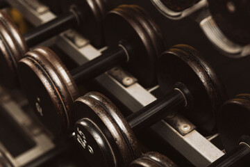 Rows of black iron dumbbells on a rack in gym, black  with white weight numbers