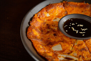 Traditional Korean kimchi pancake on the dark plate with pancake sauce on the black table vibe background
