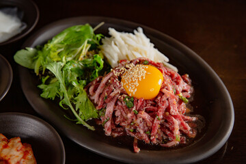 Korean Grilled BBQ combo sets with egg yolk beef tartare with pickle salad on the dark plate and black table vibe background, and pickle dishes