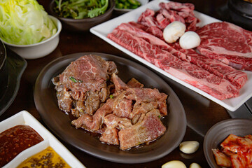 Korean Grilled BBQ combo with wagyu and marinated beef set on the traditional grill table, with lettuce, dipping sauce, rice and pickle dishes