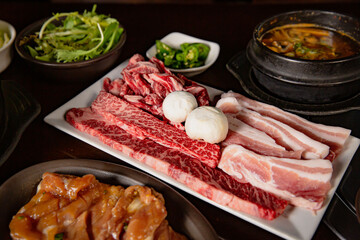 Korean Grilled BBQ combo with pork belly, wagyu and marinated chicken set on the traditional grill table, with lettuce, dipping sauce, soup and pickle dishes