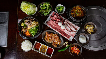 Top view of Korean Grilled BBQ combo sets on the traditional grill table, bibimbap, pork belly,...