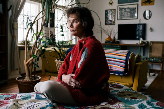 Depressed senior woman sitting alone on bed at home