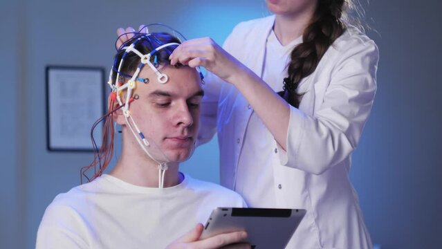 Man wearing EEG topographer for examining brain, doctor making electrogram of scalp activity. Researching of brain work using electroencephalography headset.