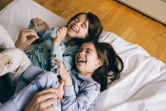Twin girls laughing while lying on bed at home
