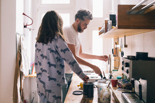Girl looking at father washing dishes at sink in kitchen