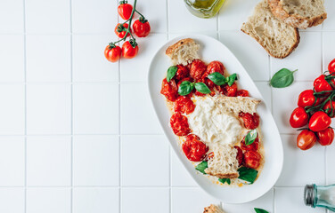 Salad with baked tomatoes and burrata on white tile background. Italian cuisine. Healthy eating....