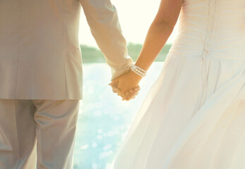 Beautiful wedding couple, bride and groom holding hands together on sea background