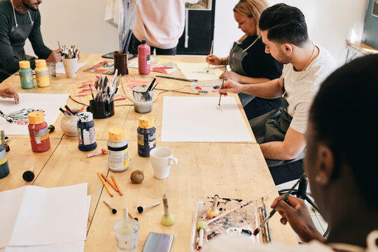 Male and female students practicing painting while sitting at table in art class