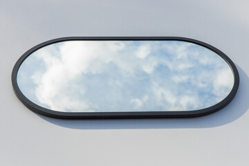 A round or oval mirror with a reflection of the blue sky and white clouds. Close-up. Isolated on a...