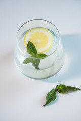 Glass cup containing mineral water with lemon and mint on white background. Refreshing drink based on lemon and mint. Tasty and healthy lemonade.