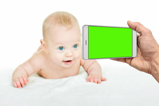 parent hand taking photo of cute little baby in bed with smartphone, blank green chromakey screen