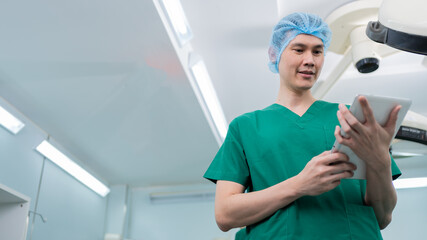 Obraz premium Portrait of Asian surgeon with medical mask standing and holding a tablet in operation theater at a hospital. Team of Professional surgeons. Healthcare, emergency medical service concept