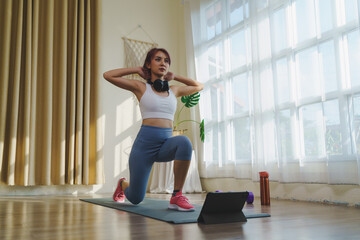Fototapeta na wymiar Fitness course at home with Technology tablet online, Asian female in sportswear and sneakers exercising indoors to burn fat, making body strong on yoga mat, Healthy lifestyle at home.