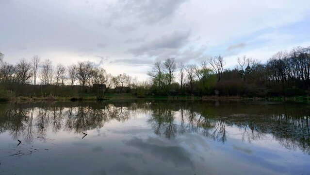 Time lapse footage of clouds passing over still pond in middle of woods creating perfect symmetrical reflection almost like a mirror.
