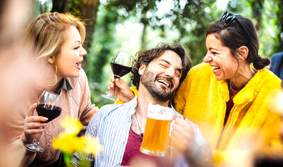 Young men and women having fun moment drinking wine and beer at garden party - Social gathering...