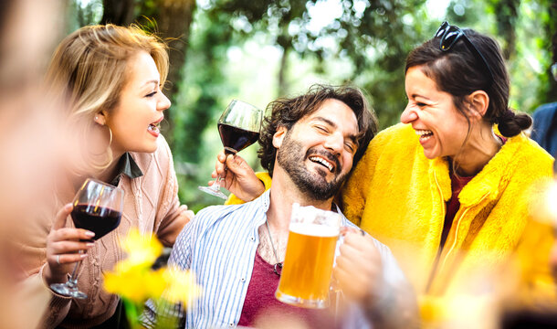 Young men and women having fun moment drinking wine and beer at garden party - Social gathering life style concept with happy people enjoying hangout time together on daytime - Bright vivid filter
