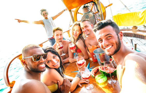 Multicultural millenial friends group taking selfie cheering at sail boat party - Summer travel life style concept with young trendy guys and girls on luxury sailboat location - Bright warm filter