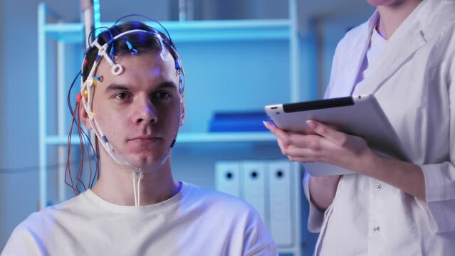 Man wearing EEG topographer for examining brain, doctor making electrogram of scalp activity. Researching of brain work using electroencephalography headset.