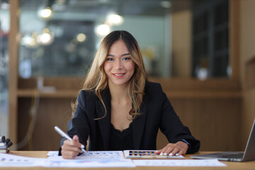 Fototapeta premium Portrait of a business woman working or secretary with laptop and financial documents on the desk in the office. Looking at camera.