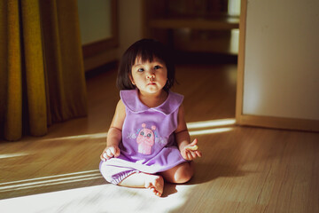 Portrait of Baby Girl wear Purple Dress sitting on the Floor in Empty room with reflection of light and shadow. Light and Shadow Concept. Looking at Camera.