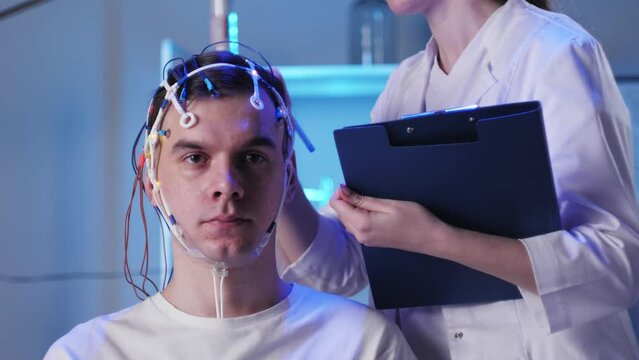 Man wearing EEG topographer for examining brain, doctor making electrogram of scalp activity. Researching of brain work using electroencephalography headset.
