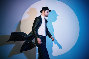 Handsome man in black coat and hat walking like superhero in the spotlight - obrazy, fototapety, plakaty
