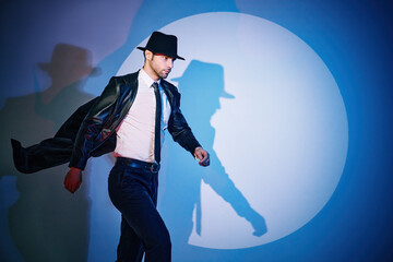 Handsome man in black coat and hat walking like superhero in the spotlight