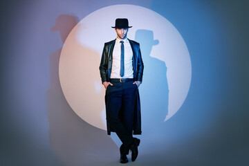 Full length portrait of handsome man in black coat and hat posing on studio in the spotlight - obrazy, fototapety, plakaty