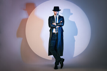 Full length portrait of confident handsome man in black coat and hat with crossed arms posing on studio in the spotlight. - obrazy, fototapety, plakaty