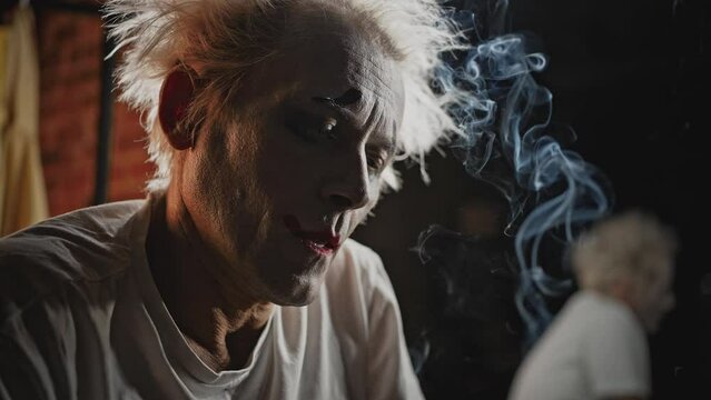 Depressed mime with tousled hair smokes in dressing room