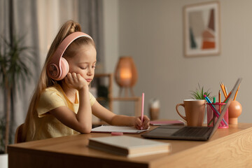 Tired Schoolgirl Learning Online Using Laptop And Taking Notes Indoor