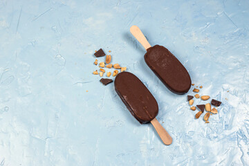 Broken chocolate ice cream bar with sticks. Chocolate popsicles with nuts on pastel blue...