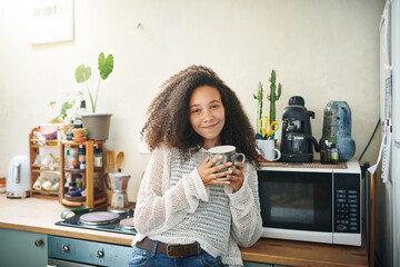 Portrait of a friendly young woman drinking coffee early in the morning